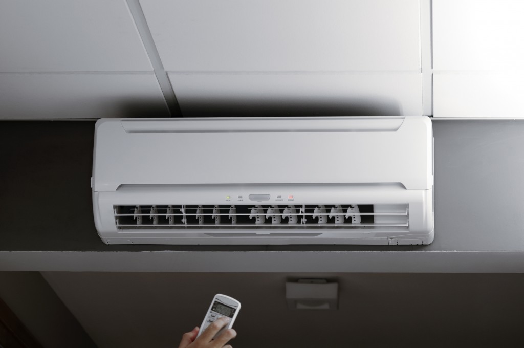 This photograph represents a hand holding a remote controller of an air conditioner